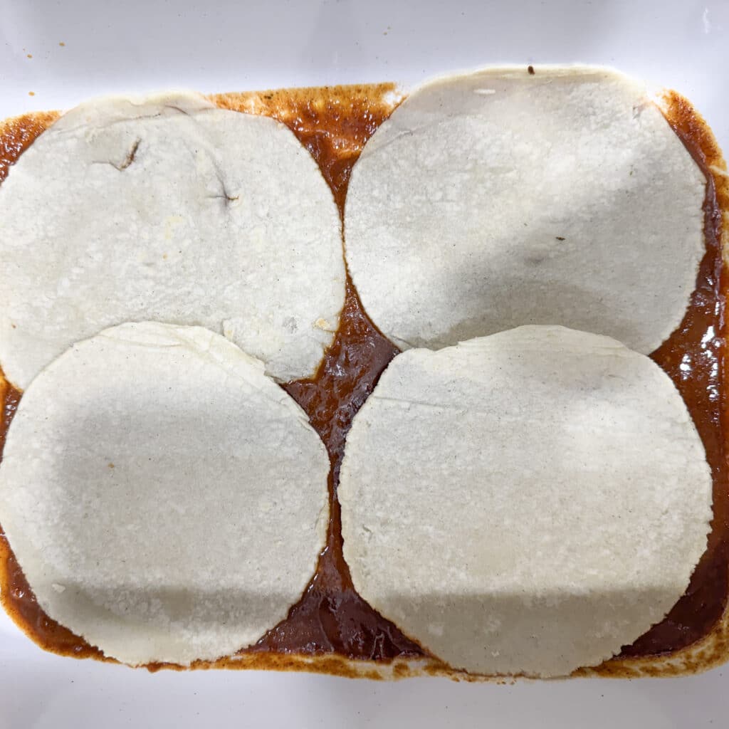 Corn Tortillas on Top of Enchilada Sauce for Chicken Enchiladas with Cream Cheese