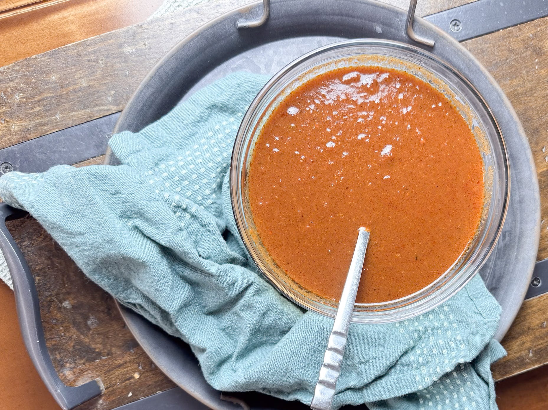 Enchilada Sauce in Bowl with Spoon and Blue Towel On Metal Plate