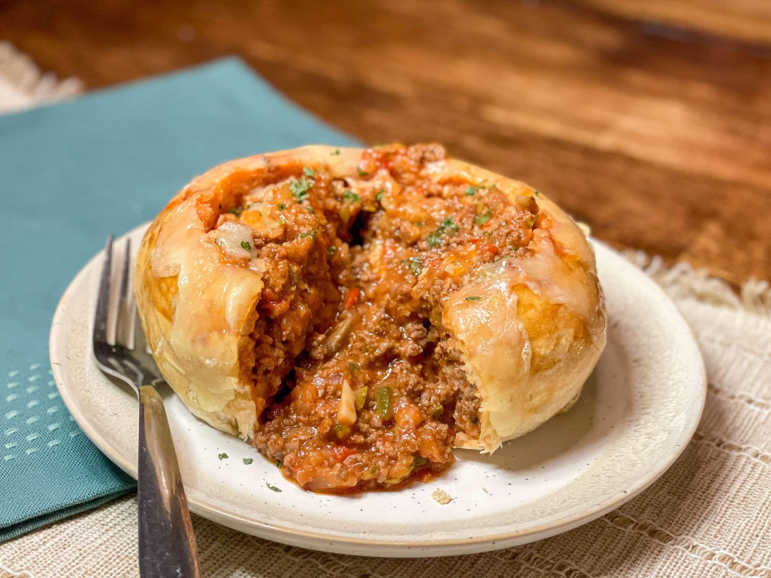 Sloppy Joe sauce oozing out of a bread bowl on a tan plate