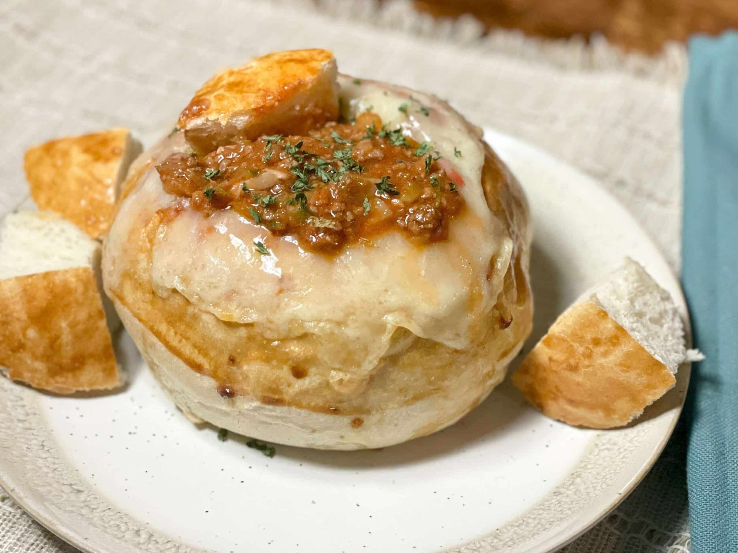 Bread bowl filled with sloppy joe sauce with pieces of bread on a white plate
