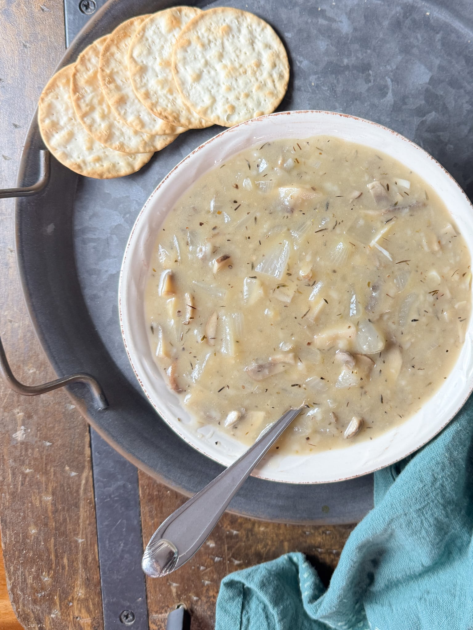 Cream of Mushroom Soup in a Bowl with a spoon on a Metal Plate and some crackers next to it