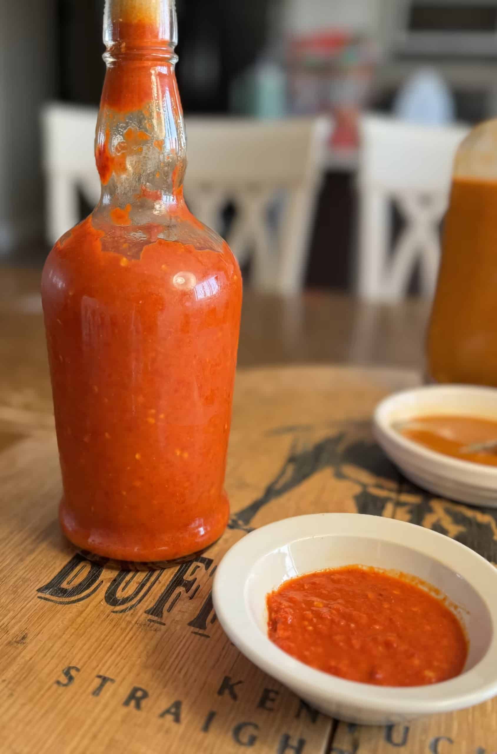 Cayenne Hot Sauce in Small Bowl with Bottle Behind It