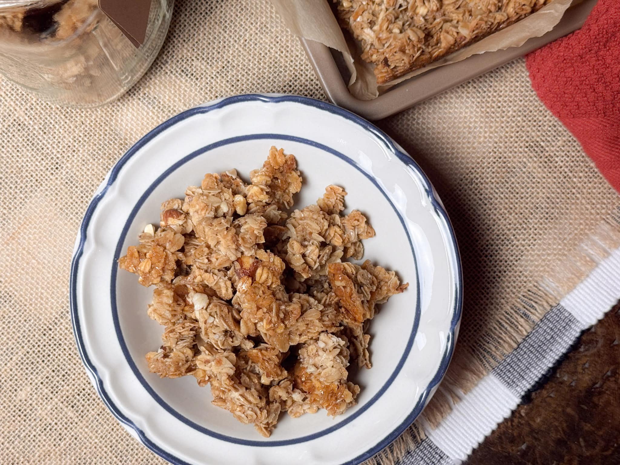 Honey Oat Granola In a White Bowl with Blue Rim and a sheetpan of granola in the background