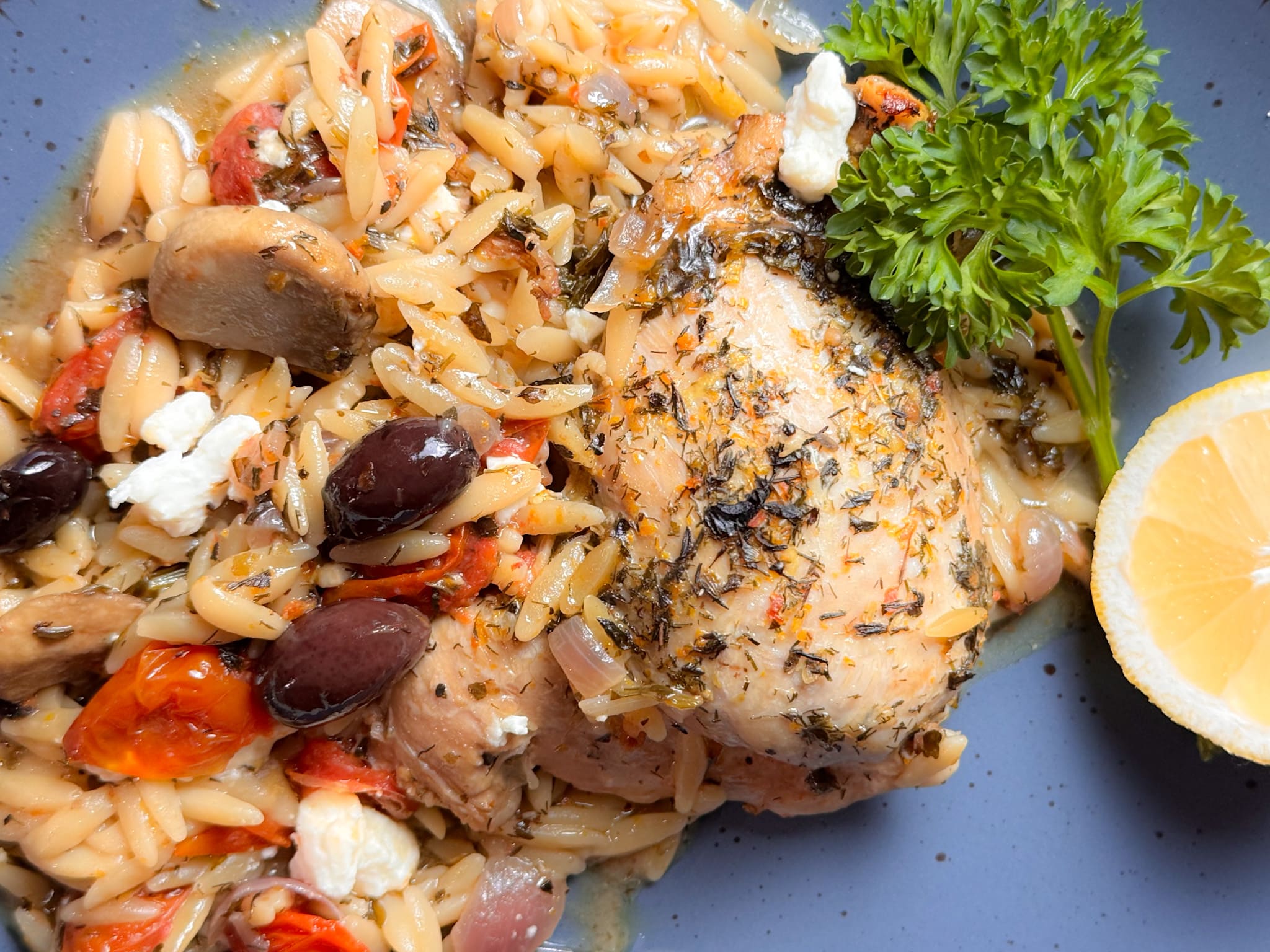 One Pan Mediterranean Chicken and Orzo on Blue Plate With Half a Lemon and Parsley Garnish