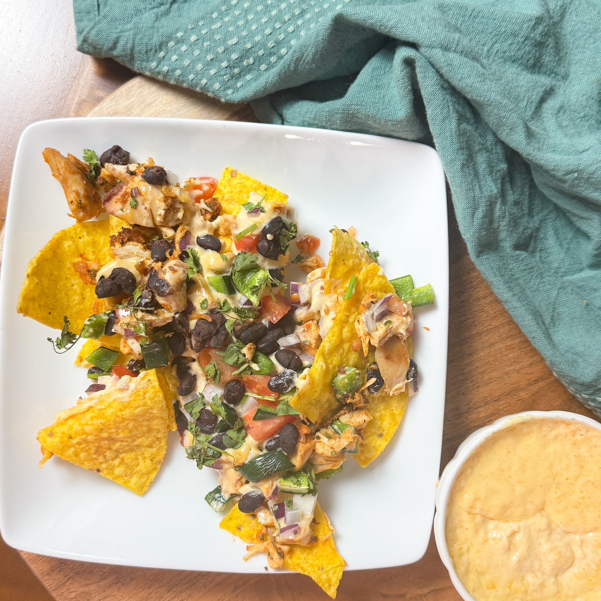 Smoked Chicken Nachos on a white plate with nacho cheese in a bowl next to it and a green napkin