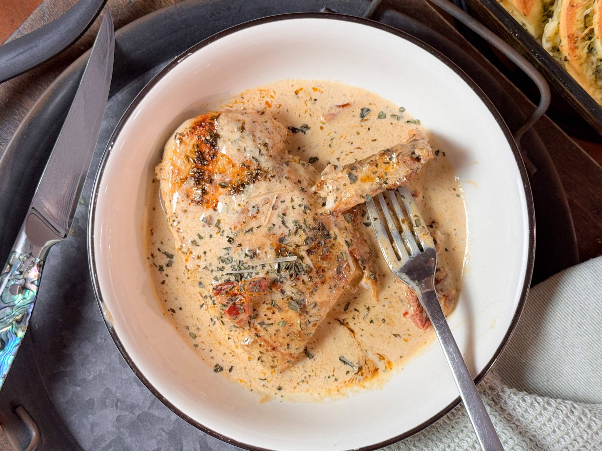 Sundried Tomato Chicken smothered in Garlic Parmesan Sauce, a Fork with a piece of chicken on it, all in a White Bowl