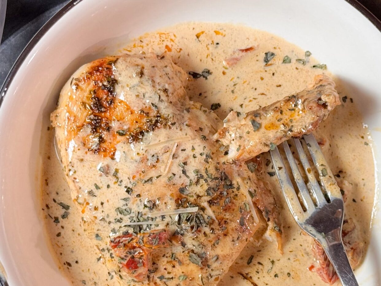 Sundried Tomato Chicken Smothered in Garlic Parmesan Sauce, a Fork with a Piece of Chicken on It, All in a White Bowl