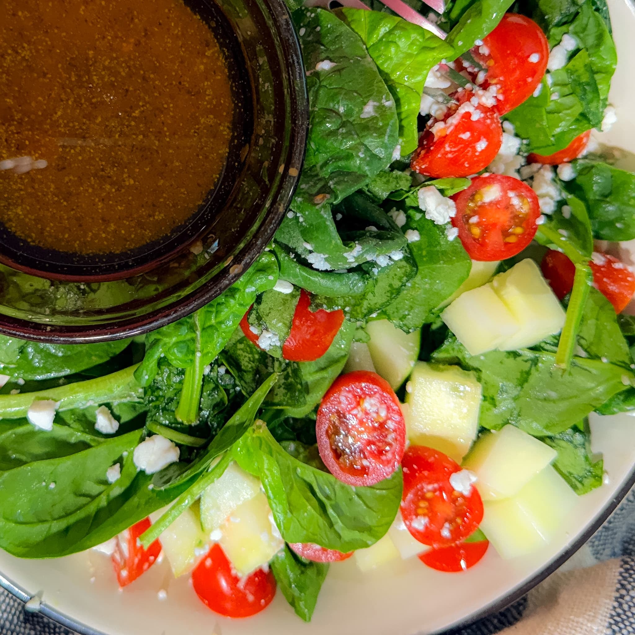 Overhead View of Fresh Spinach Feta Salad with Cherry Tomatoes, Chopped Cucumber and Crumbled Feta Cheese Served with Balsamic Vinaigrette.