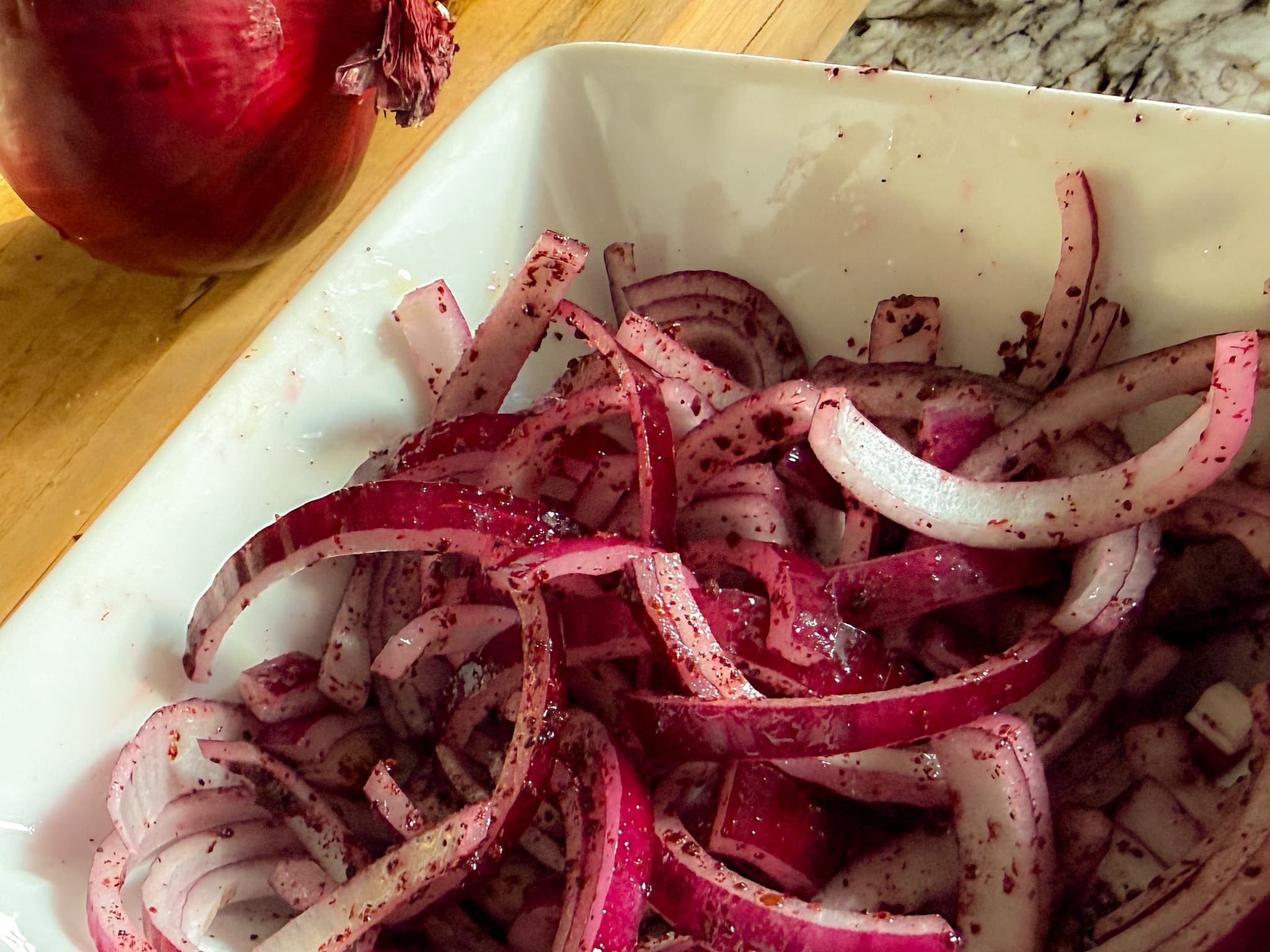 Close-up of Thinly Sliced Red Onions Coated with Purple Sumac Seasoning and Olive Oil, Ready to Serve with Gyros.